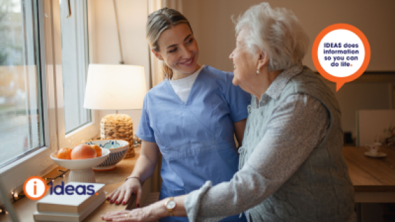 Image of an elderly person and a carer, standing at a kitchen bench.