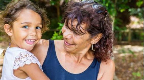 Image of smiling Aboriginal woman holding a young child in her arms.