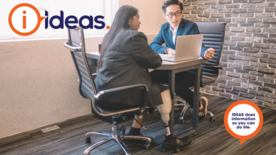 A woman with prosthetic leg and man, both seated at a desk are looking at a computer.