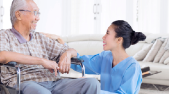 Aged care support worker crouching down to talk with a wheelchair user.