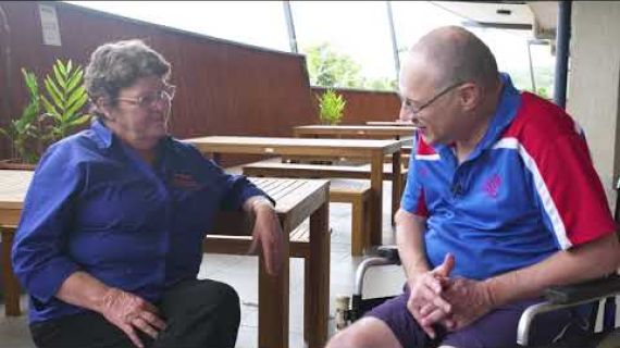 Man sitting in a wheelchair with lady sitting on a bench talking