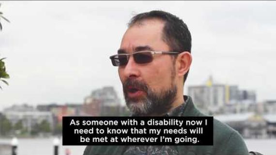 Man sitting in wheelchair with city and water backdrop speaking about travel and disability