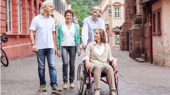 friends moving down a cobbled street. One person is a wheelchair user. All are smiling and talking.