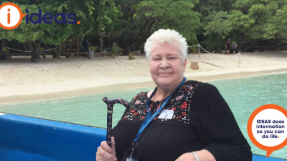Mother in Law seated in a boat, with her cane, behind her is the shoreline.