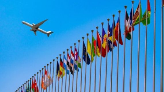 Image of aeroplane flying over row of international flags