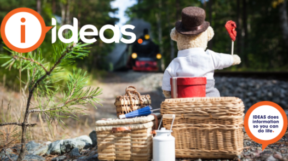 Concept photo of travel. A teddy bear sits on top of woven baskets signalling a steam train to stop. He has a hat box, pail and umbrella.