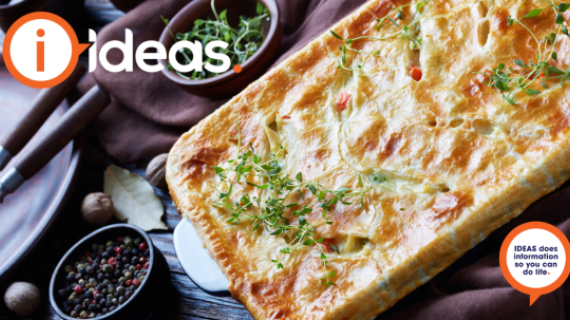 A table set with a pie dish, cutlery, crockery and a nutmeg, bayleaf and peppercorns. The pie is golden with vegetables showing through some slits, it is garnished with herbs such as thyme.