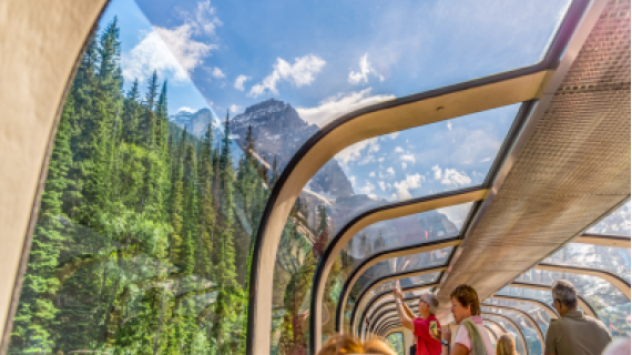 An image of the Canadian Rocky Mountains viewed from inside a train with a glass roof.