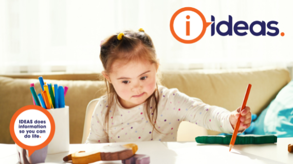 Young girl sitting at a table, drawing on a piece of paper with an orange pencil.