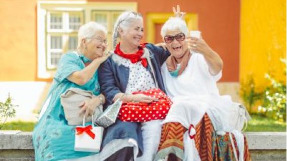 Image of three senior ladies. One is holding a phone and they are all smiling for a selfie photo