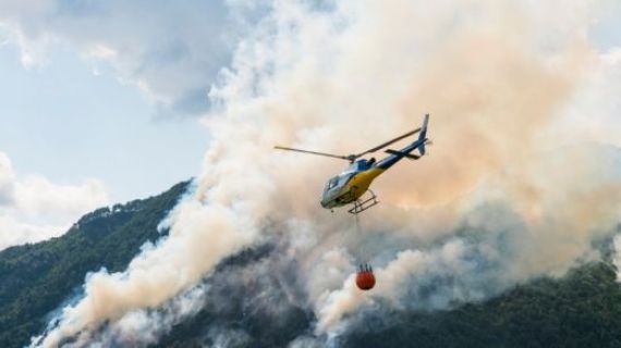 Helicopter with a bucket attached flyer over hills that are on fire