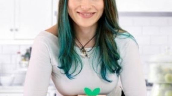 A woman with dark and green hair, smiling and sitting behind a Mashblox product display