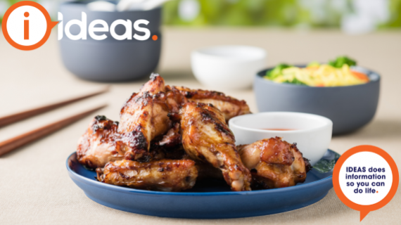 Cooked chicken wings served on a plate. To the side are chopsticks and some condiment bowls.