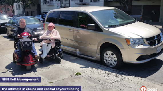 A couple infront of an accesible vehicle in San Fransisco, they are both seated, Carolyn in a wheelchair, Steve in an motorised scooter