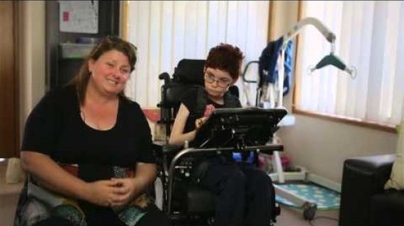 Young girl in wheelchair sitting next to her mum