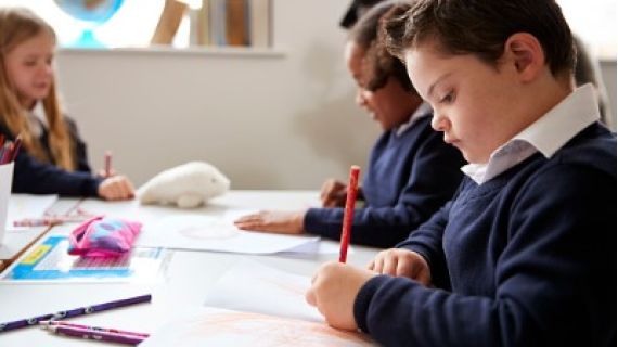 Preteen school boy with down syndrome working a desk in a classroom with a pencil in hand