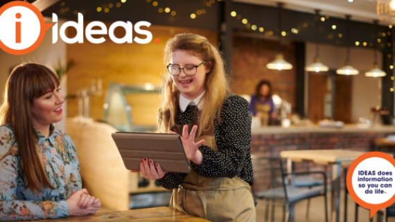 Two women in a coffee shop. One with disability is using a device to take the customers order.