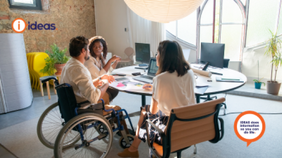 A wheelchair user and 2 other people siting at a table discussing work..