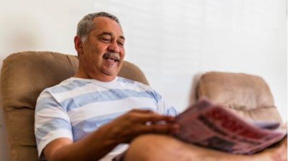 Image of smiling Aboriginal man sitting on a couch with his leg crossed.