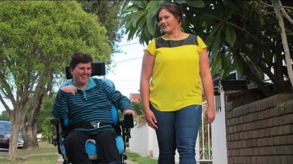 Lady in a wheelchair and a friend walking by her side on the footpath