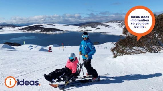 a person using a sit ski with a companion standing on skis behind