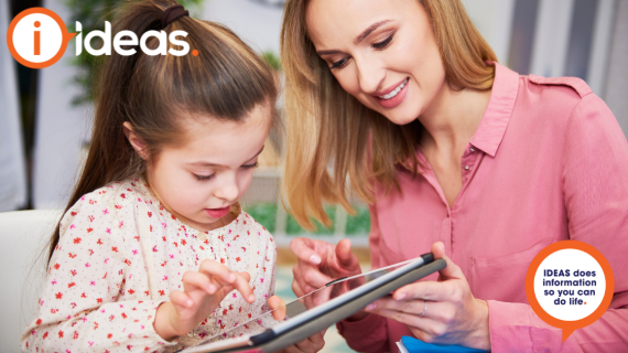 Mother helps a female toddler use an ipad.