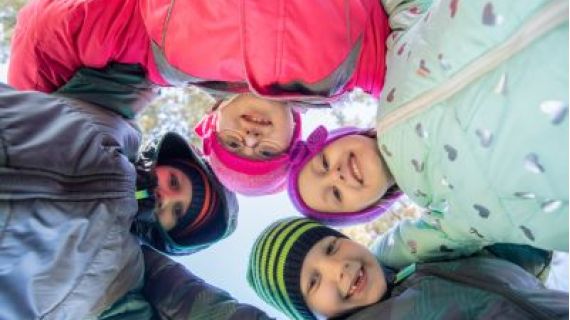 Children, one with disability, in a circle looking down at the camera.