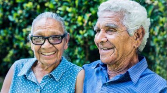 Image of smiling elderly Indigenous couple wearing blue shirts.