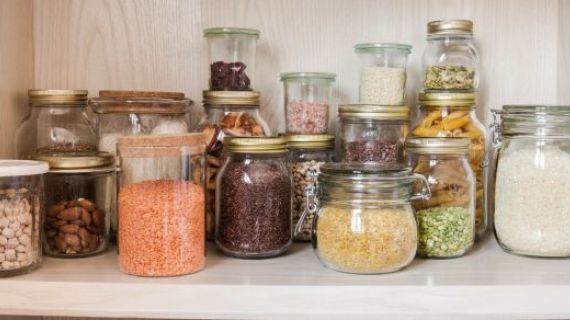 An image of a pantry shelf. Items like beans, nuts, lentils, rice, and pasta are stored in glass jars.
