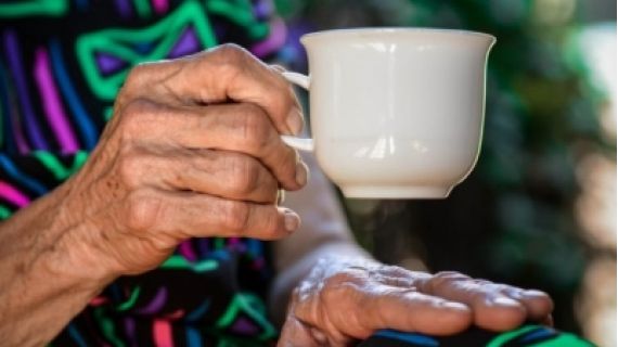 Image of an aged woman's hand holding a white cup