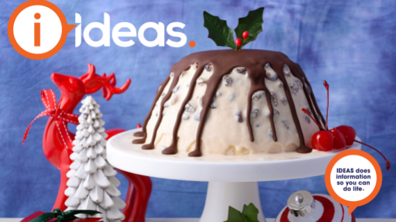 An ice-cream Christmas Pudding, on a plate with chocolate drizzles over the top. Christmas decorations are in the background.