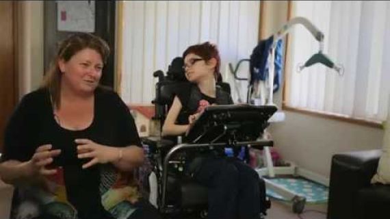 Young girl in a wheelchair sitting next to her mum