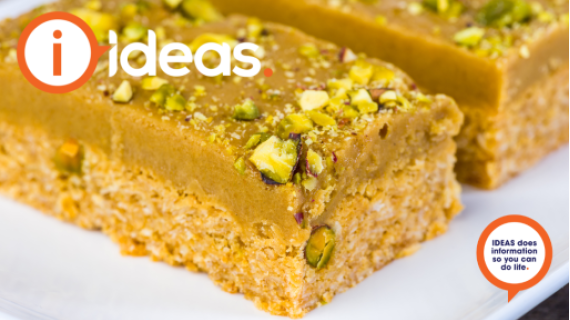 A caramel coloured slice with two layers and crumbled pistachio in the icing.