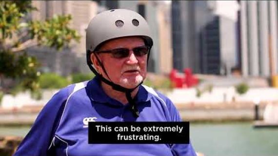 Man sitting in wheelchair with a helmet on with city background speaking