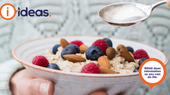 An image of a person in a light grey winter jumper. In one hand they hold a speckled bowl, inside the bowl is porridge, topped with raspberries, blueberries and almonds. In the other hand they hold a silver spoon over the bowl.