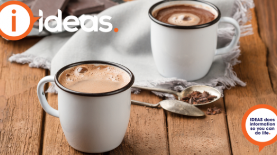 Two mugs of hot chocolate, two spoons and a napkin with pieces of chocolate in the background