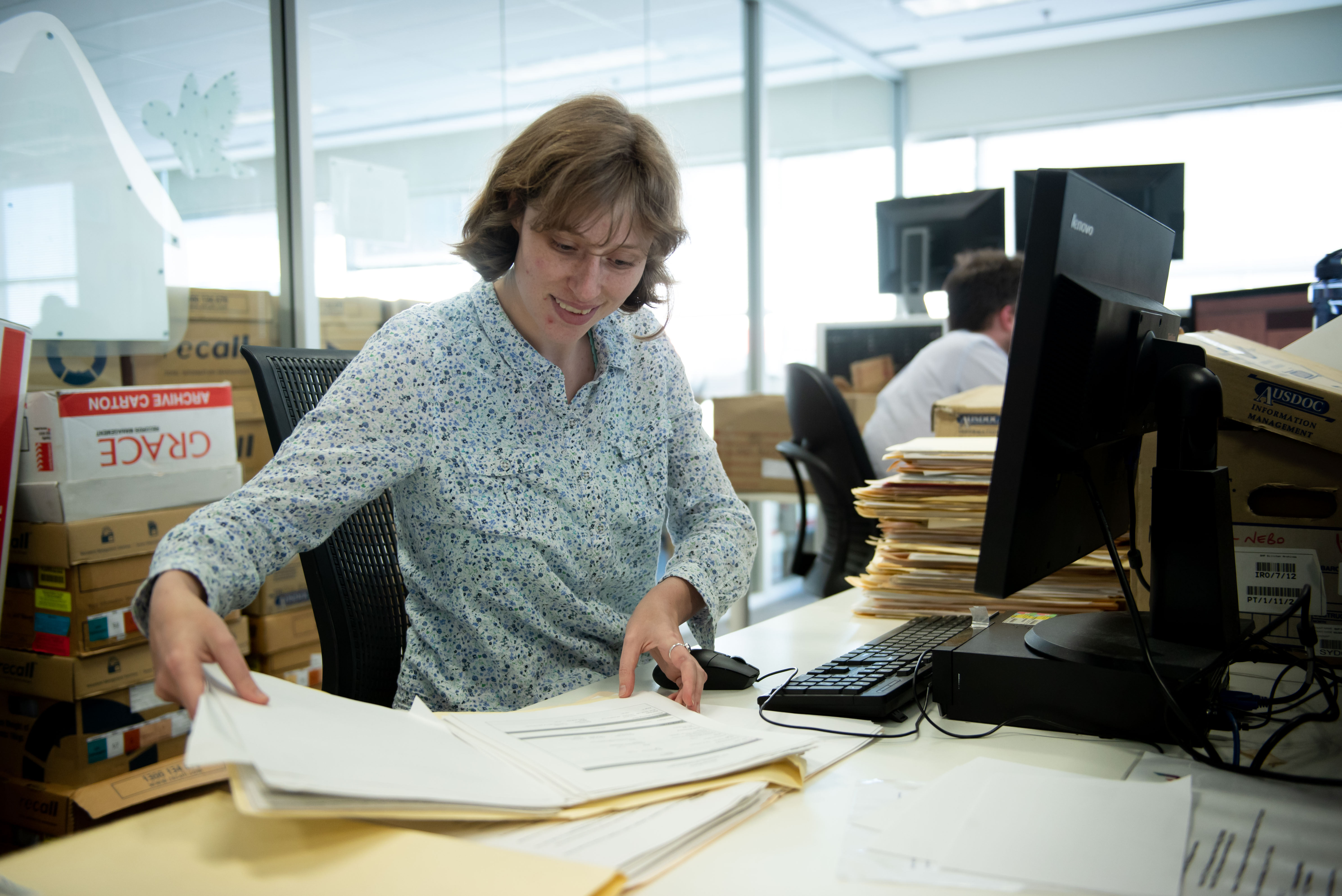 Lady refering to a file , sitting in front of a desktop