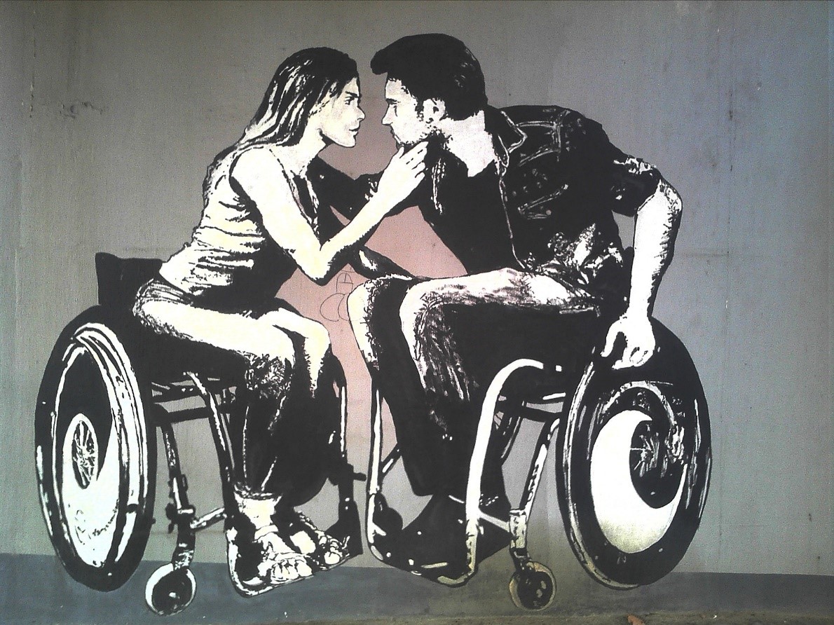 A man and a lady sitting in separate wheelchairs sharing an intimate moment kissing