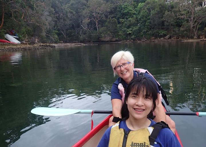 Two women in a boat in a river. Both smiling, one is holding an oar. 