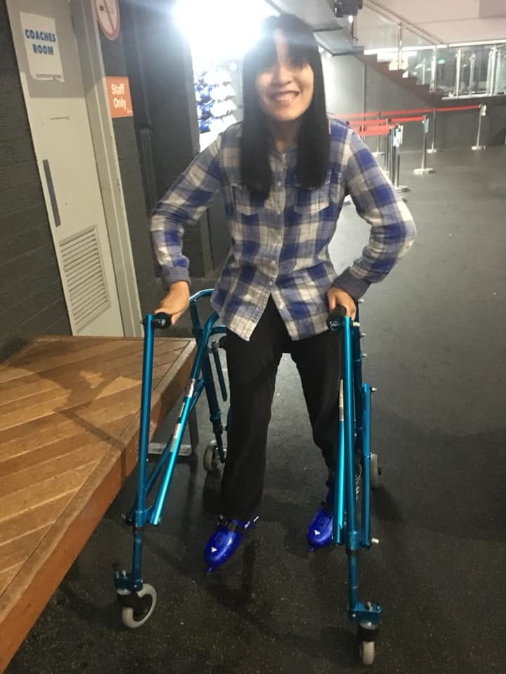 Nicole skating on an ice rink with a mobility aid to support her.