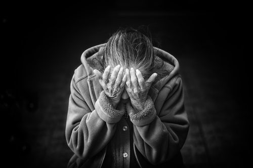 A black and white photo of an older person is neatly dressed leading forward with their face in their hands