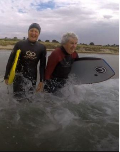 Two people walking into the ocean with boogie boards